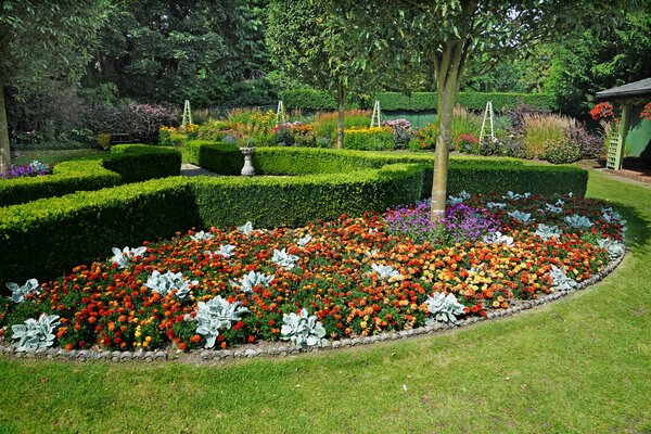 Ein gepflegtes Blumenbeet in einem formellen Garten mit Hecken und bunten Blumen.